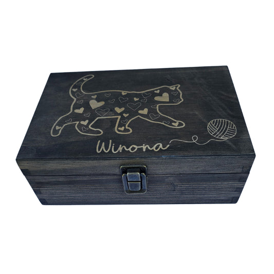 Black box with a latch. A cat with a heart with a ball of yarn. The cat appears to be moving towards the ball of yarn. Under the cat is the cat's name